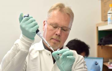 Anders Naar stands in a lab holding a pipette and test tube
