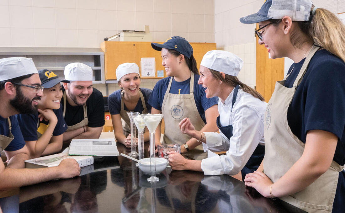 A photo of multiple people wearing hats and aprons in a kitchen