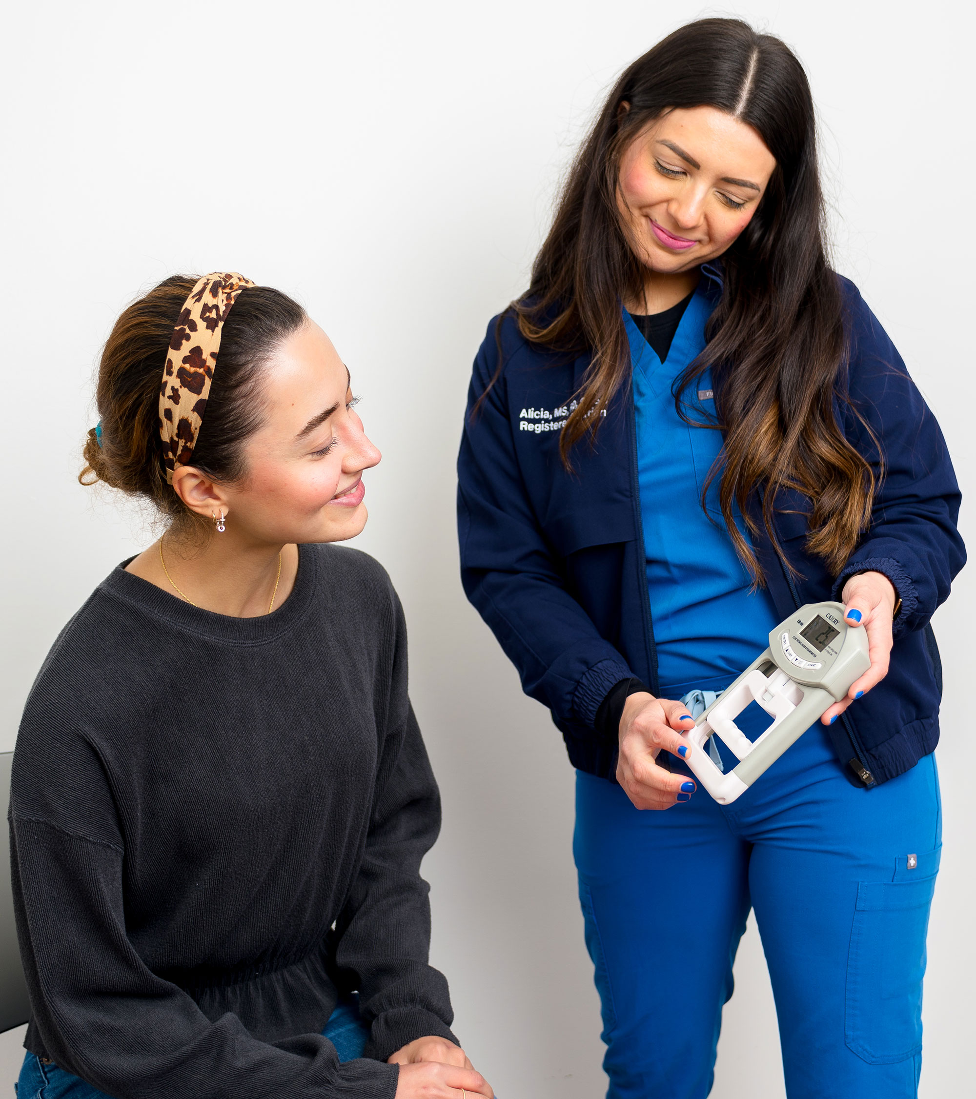 A woman in nursing scrubs showing another woman a dietetics tool