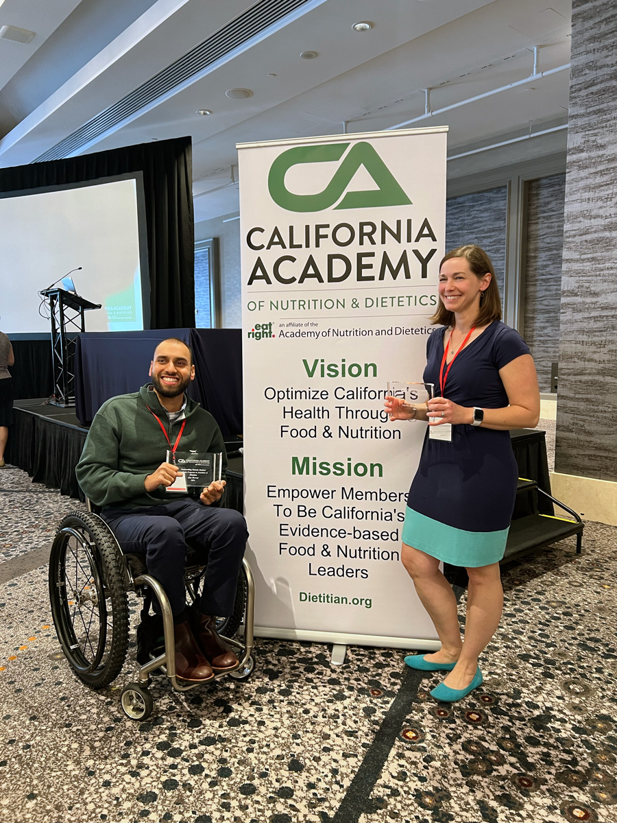 A photo of a man and a woman posing with an award in front of a banner.