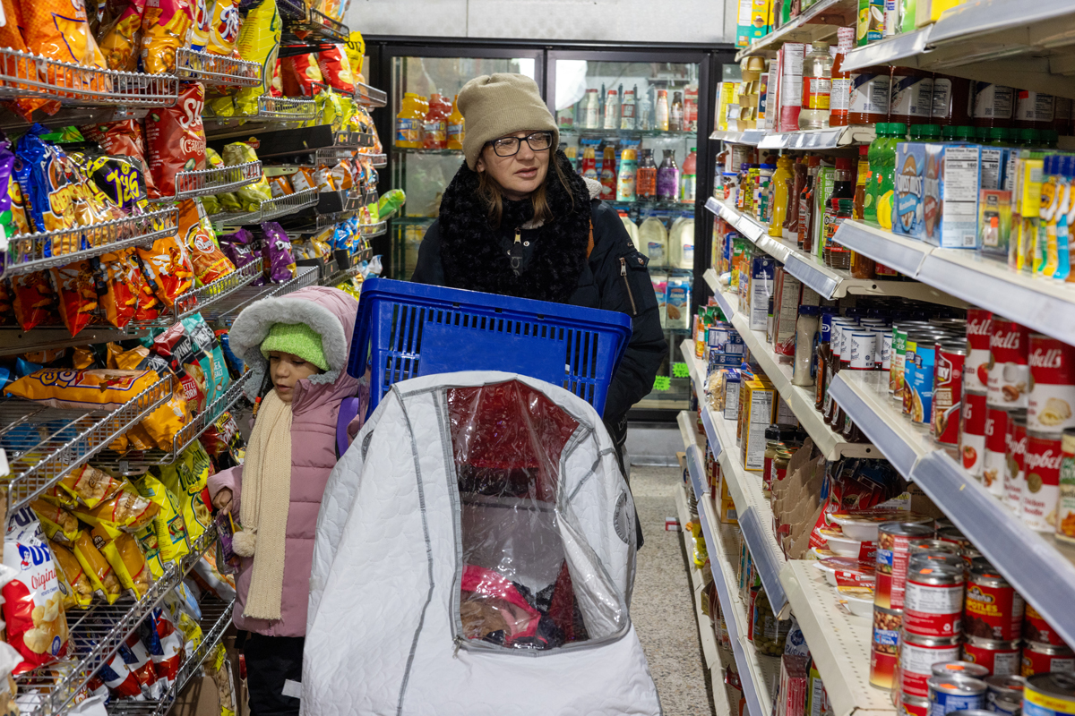 A woman and child walk through the aisles of a grocery store. Several food packages are visible on both sides of them.