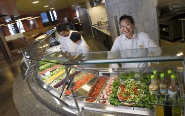 Workers standing behind an organic salad bar in a campus cafeteria